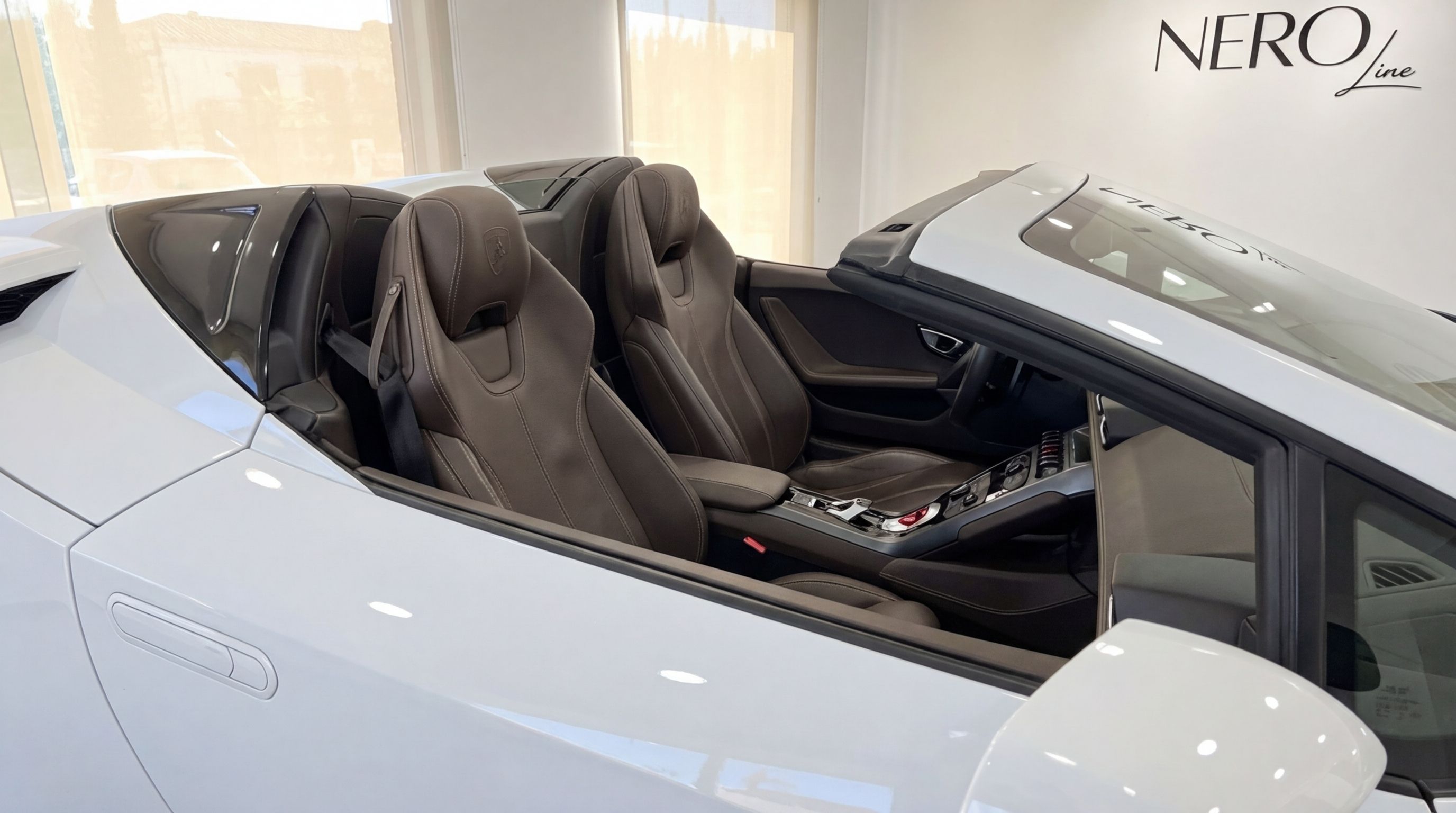 A white Lamborghini Huracan Spyder convertible with its roof down, showcasing the luxurious brown leather interior and dashboard from a side view in Valencia.