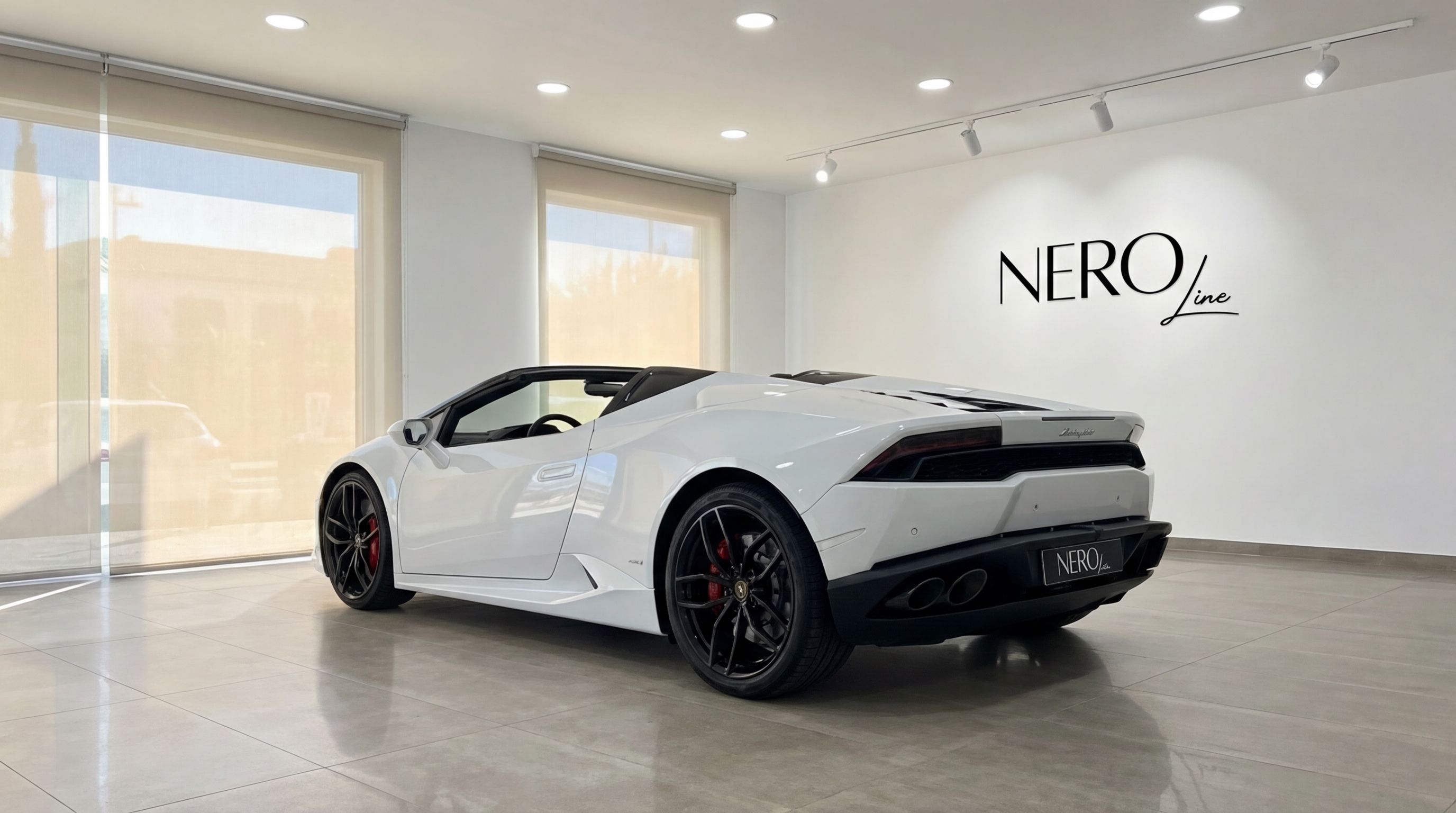 A white Lamborghini Huracan Spyder convertible, seen from the rear three-quarter angle, parked in a bright showroom in Valencia.
