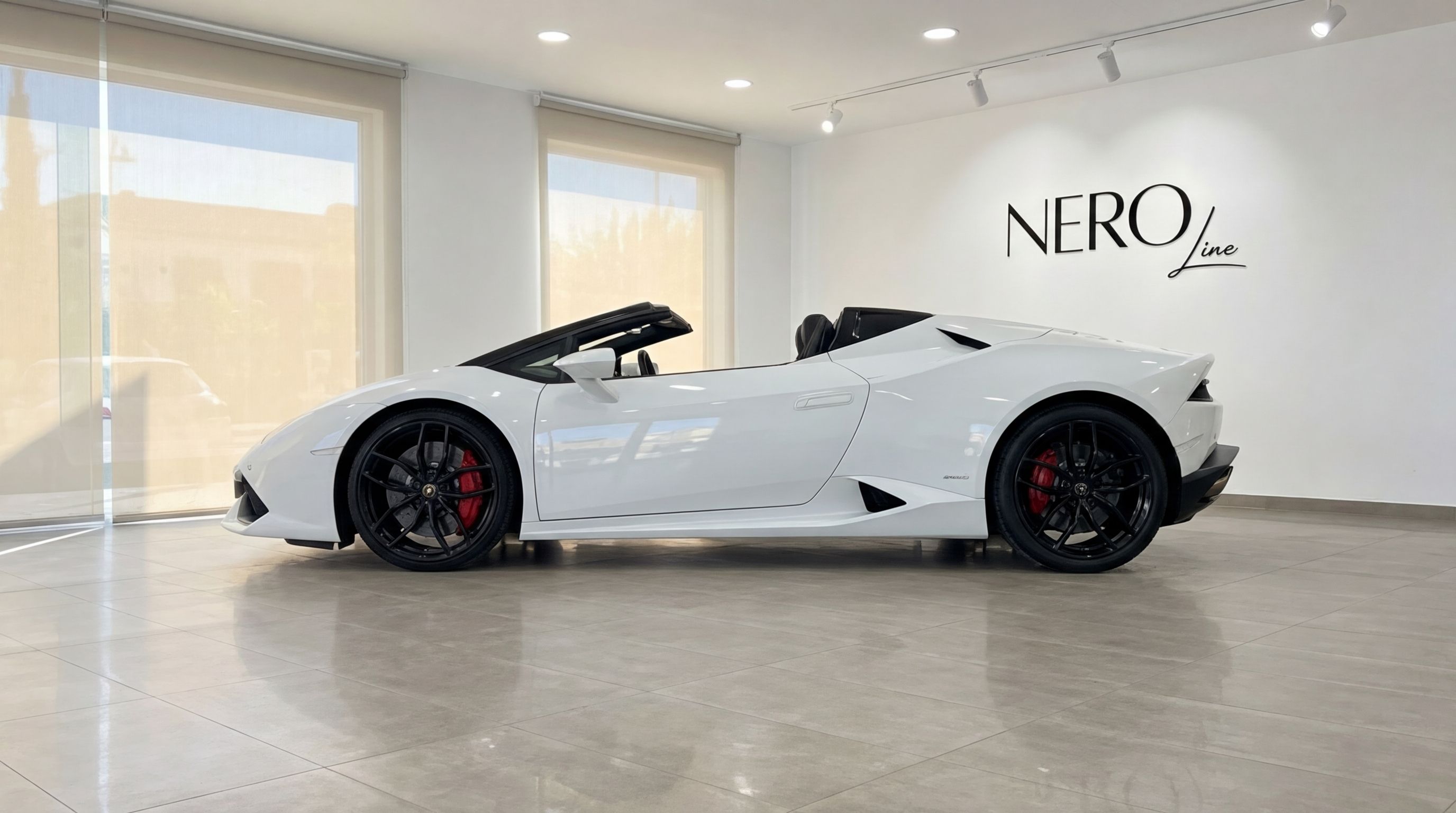 A sleek white Lamborghini Huracan Spyder convertible is showcased from a side view with its top down in a modern Valencia showroom.