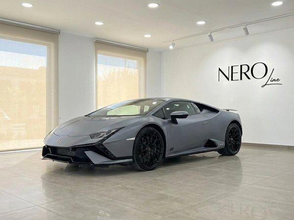 Lamborghini Huracan Tecnica — Showroom en Madrid Un Lamborghini Huracan Tecnica 2025 gris mate se exhibe desde una vista tres cuartos frontal en un luminoso showroom de Madrid con el logo de Nero Line.