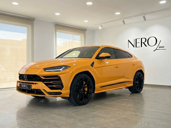Lamborghini Urus S — Front view Barcelona showroom The orange Lamborghini Urus S is showcased from a front three-quarter view in a bright showroom in Barcelona.