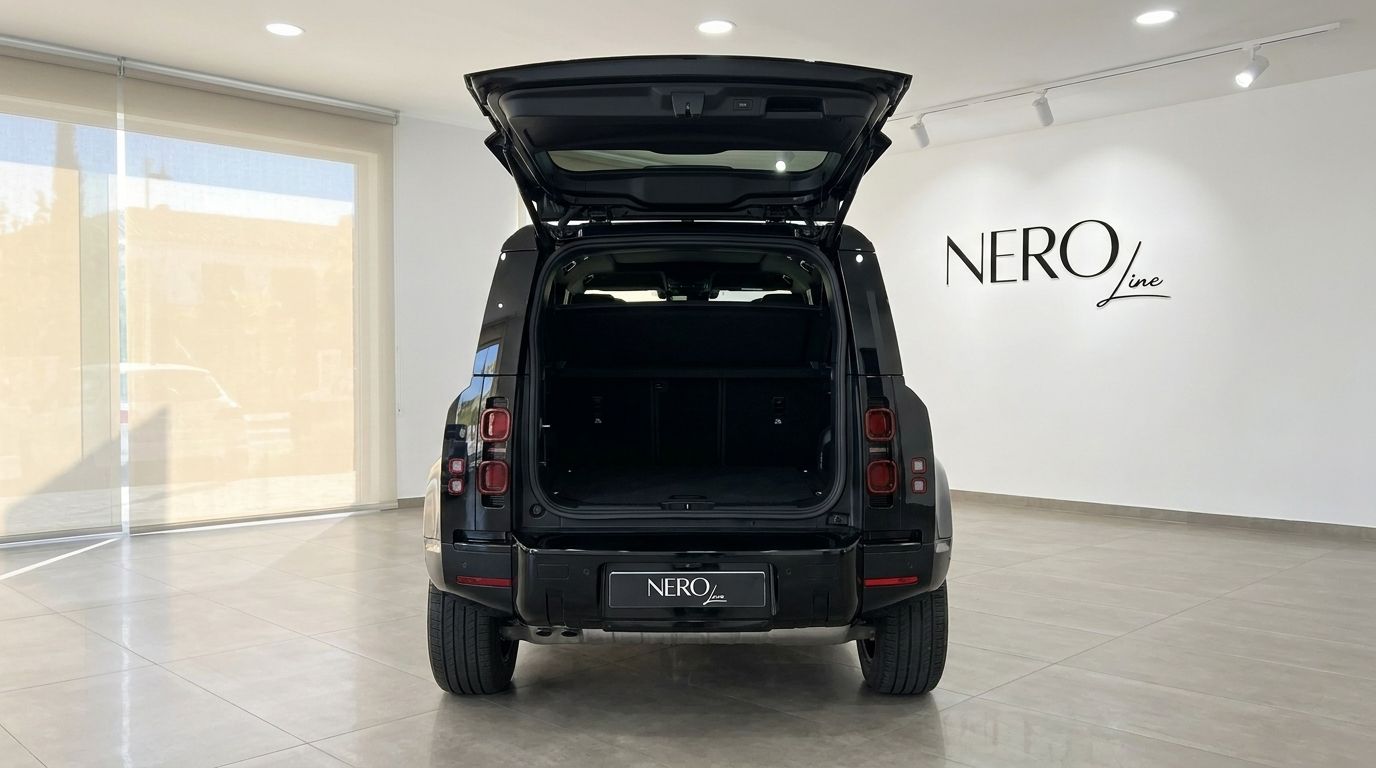 A black Land Rover Defender 2025 shown from the rear with its boot open, revealing the spacious cargo area in a Madrid showroom.