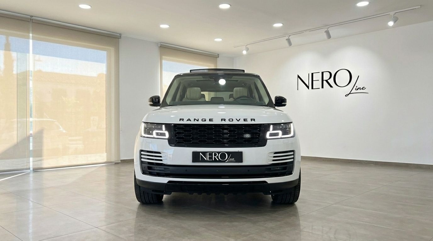 The white Land Rover Range Rover Vogue is showcased head-on in a bright showroom in Alicante, featuring its distinctive grille and headlights.