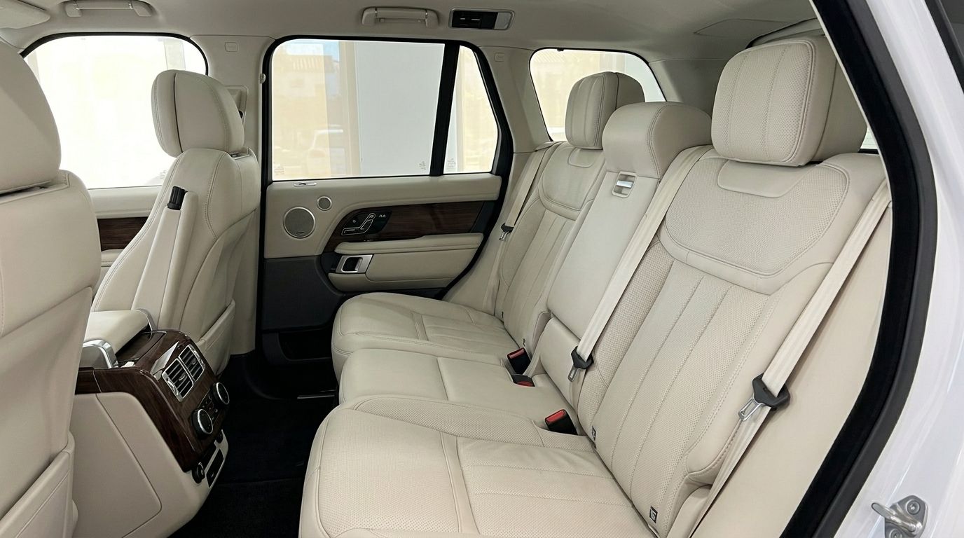 The luxurious rear interior of the Land Rover Range Rover Vogue in Alicante, featuring light leather seats and wood trim.