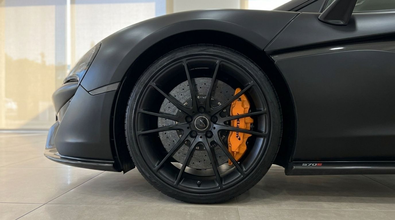 Close-up of the McLaren 570S's matte black front wheel with striking orange brake caliper, available in Marbella.