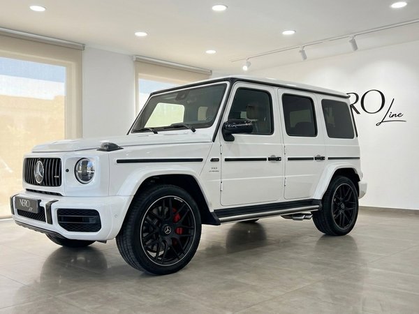 مرسيدس-AMG G 63 — سيارة دفع رباعي فاخرة في ماربيا يُعرض طراز مرسيدس-AMG G 63 الأبيض لعام 2023 من زاوية أمامية ثلاثية الأرباع في صالة عرض مشرقة في ماربيا.