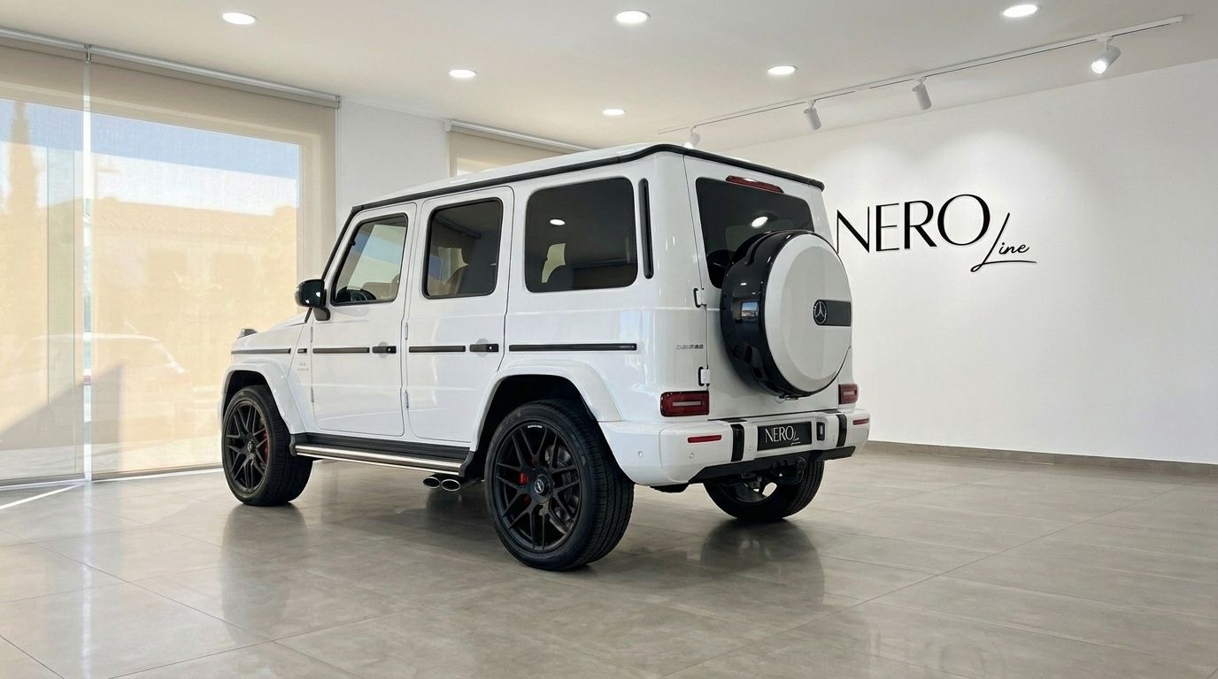 تُعرض سيارة مرسيدس-AMG G 63 بيضاء لامعة (2023) من الخلف في صالة عرض بماربيا، مع عجلتها الاحتياطية الأيقونية وعجلاتها السوداء.