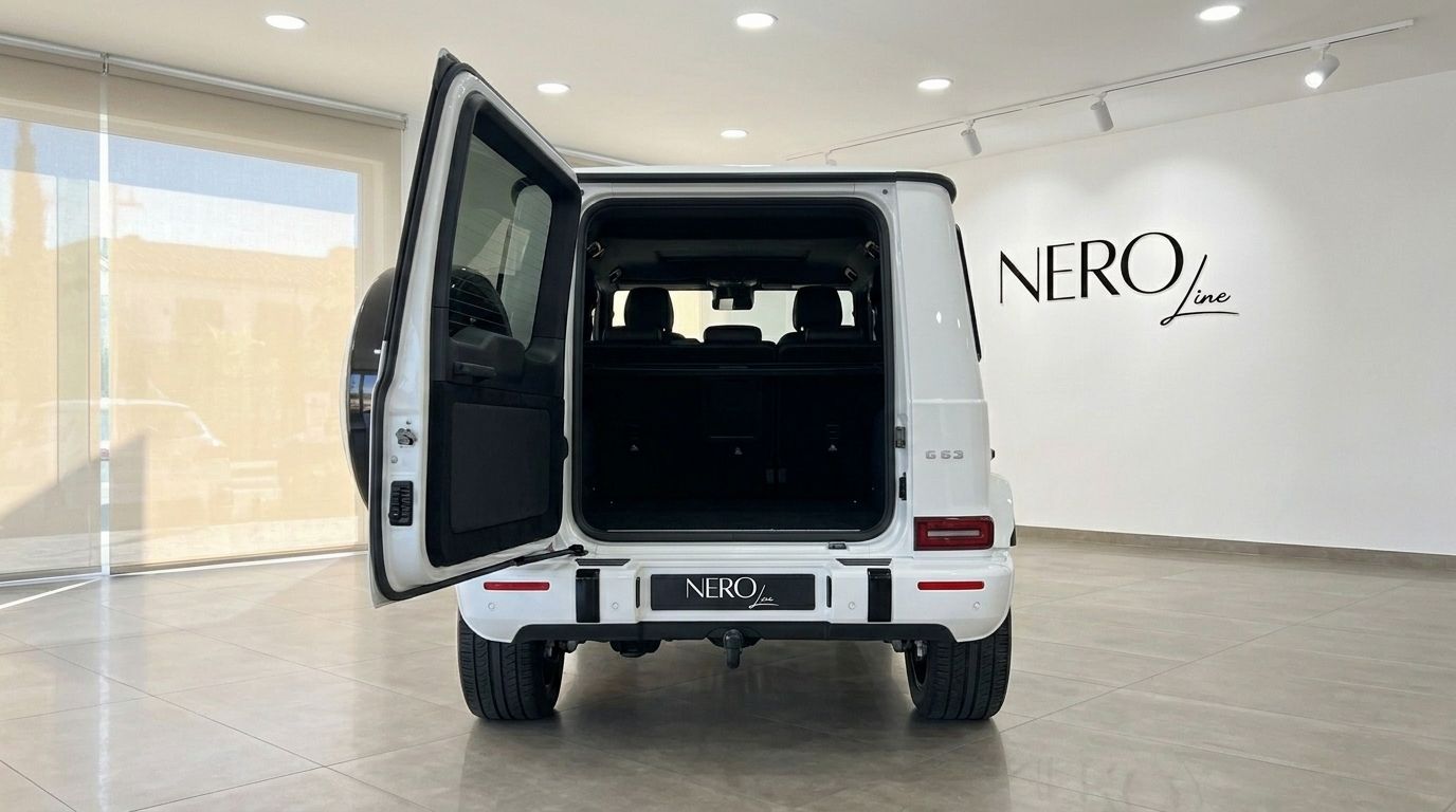تظهر سيارة مرسيدس-AMG G 63 البيضاء موديل 2023 من الخلف مع فتح صندوق الأمتعة، كاشفة عن المقصورة الداخلية الواسعة في صالة عرض ماربيا.