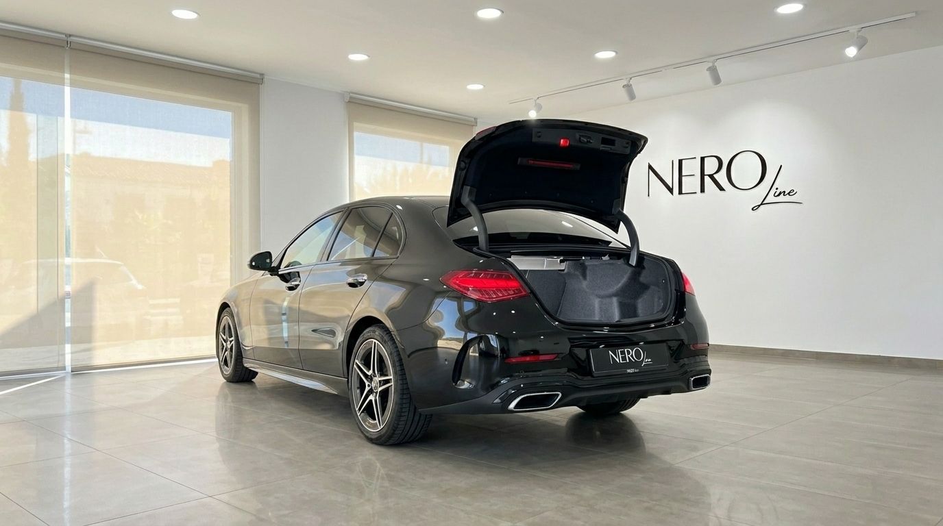 A black Mercedes-Benz C 180 is shown from the rear-three-quarter angle with its trunk open, parked in a bright showroom in Alicante.