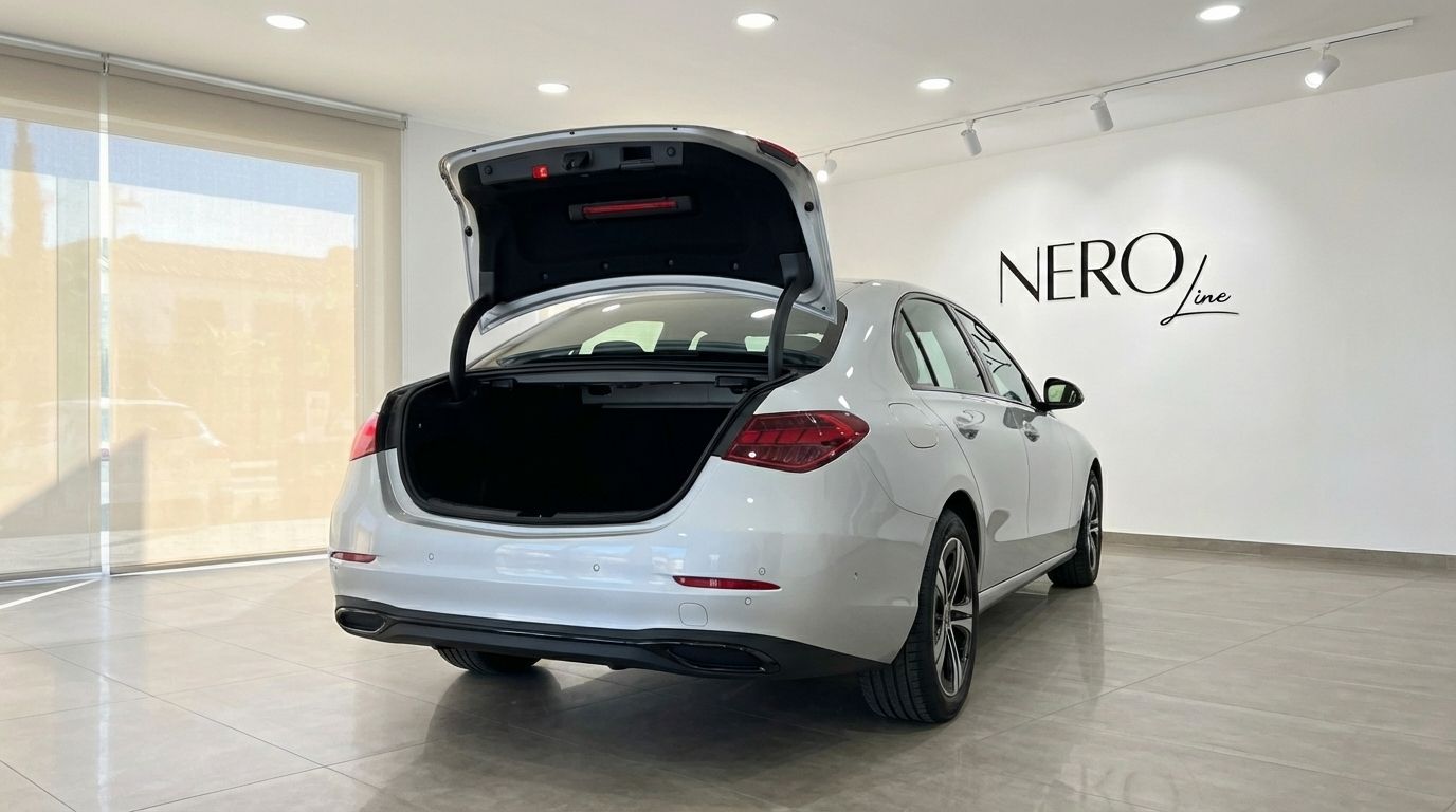 Rear view of a white 2024 Mercedes-Benz C220d with its trunk open, parked in a modern showroom in Alicante.