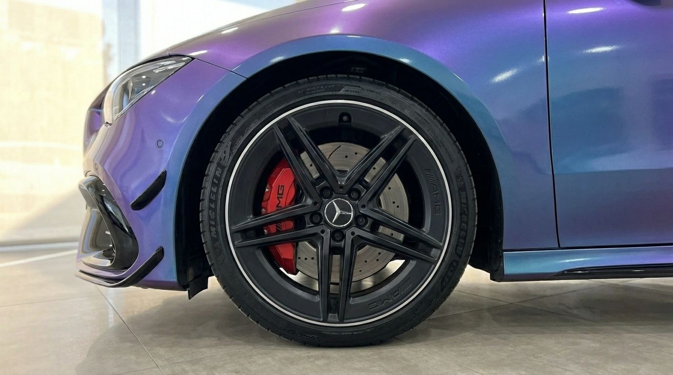 Front wheel and fender of a Mercedes-Benz CLA 45 AMG in Alicante, with a black rim, red AMG brake caliper, and iridescent paint.