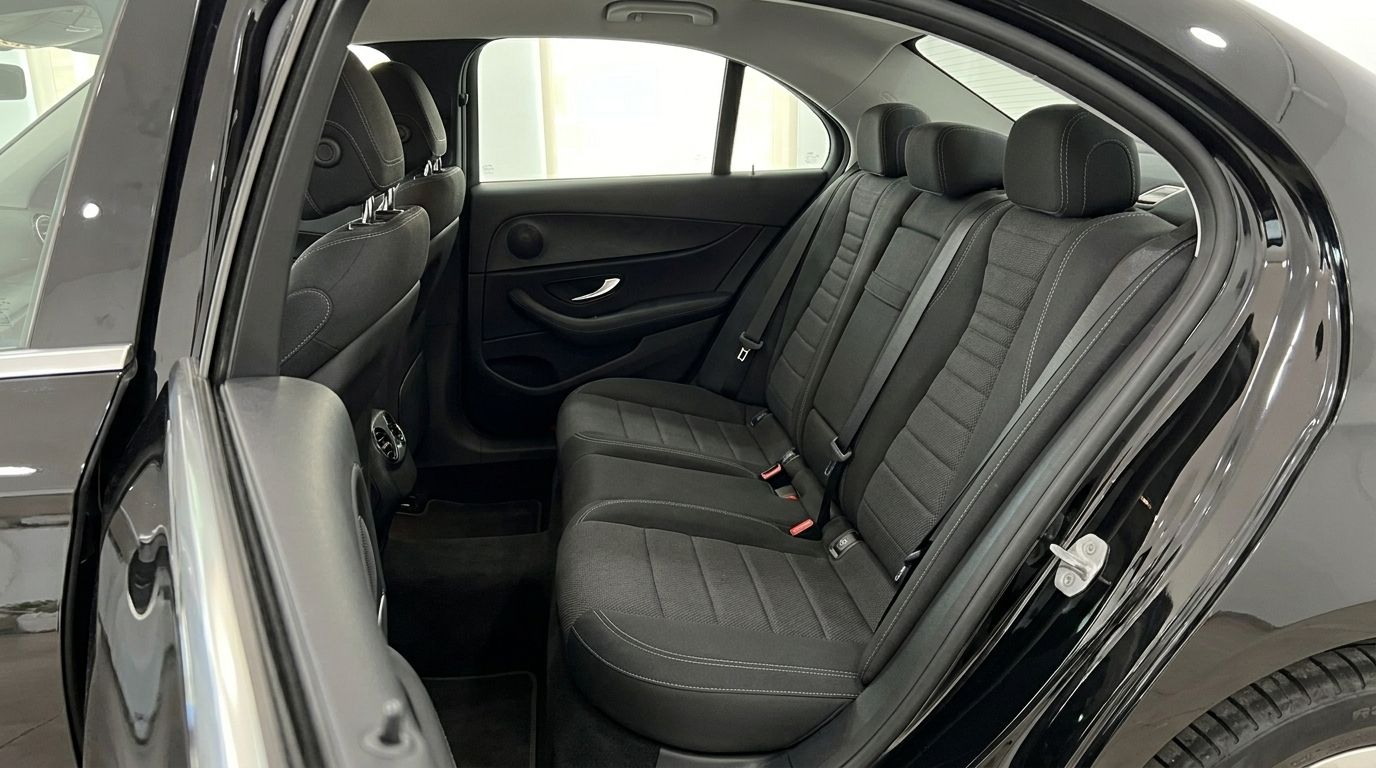 The spacious rear interior of the 2019 Mercedes-Benz E-Class, featuring dark fabric seats and door panels, available for rent in Alicante.
