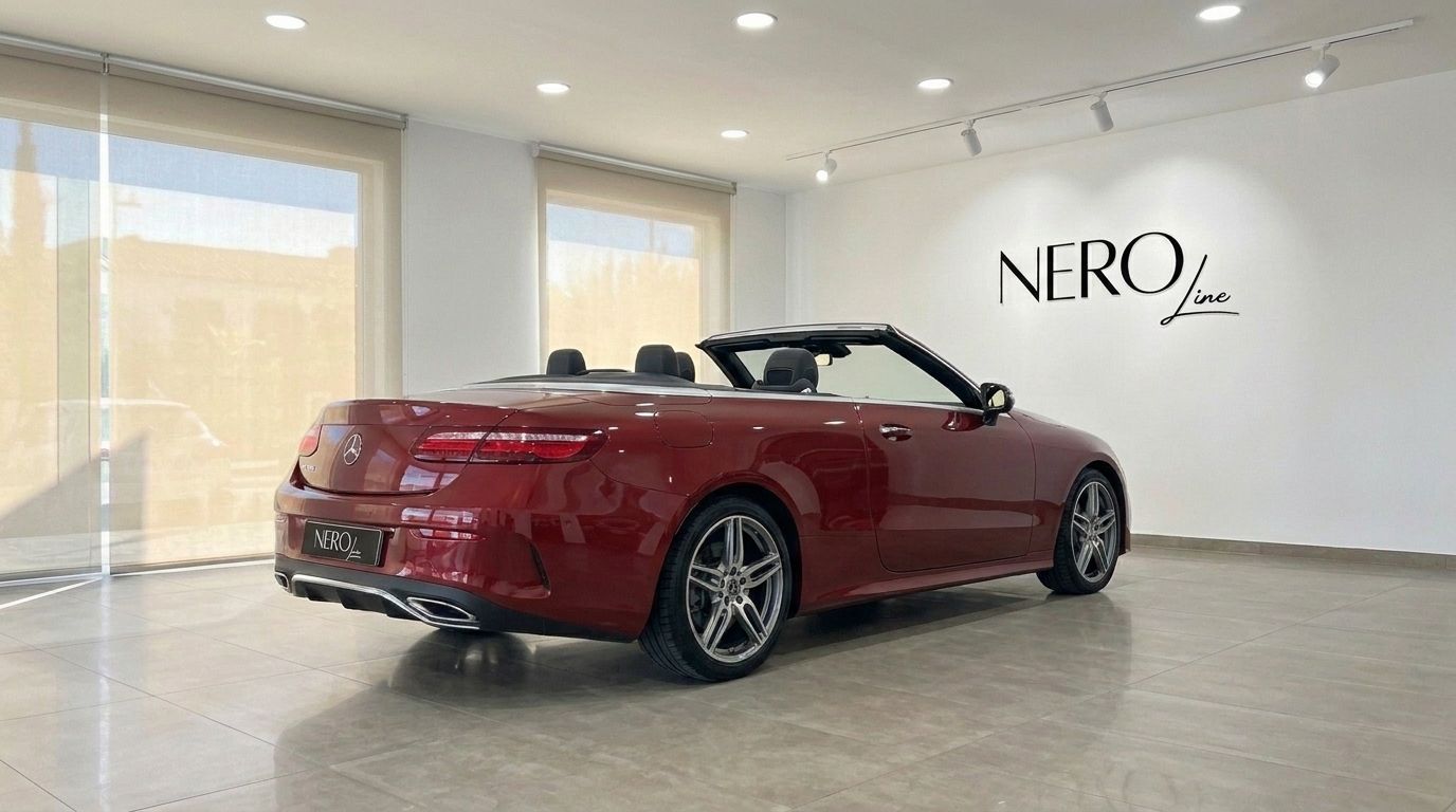 The burgundy red Mercedes-Benz E-Class Cabrio AMG Line is showcased from a rear three-quarter angle with its top down, inside a showroom in Mallorca.
