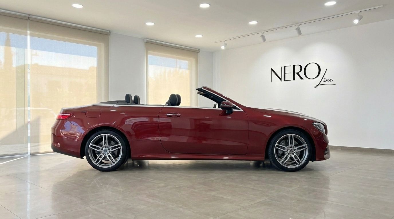 The burgundy red Mercedes-Benz E-Class Cabrio AMG Line convertible is parked sideways with its top down in a showroom in Mallorca.
