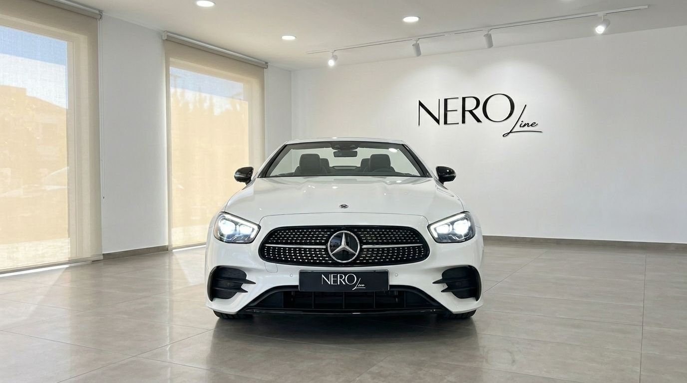 La Mercedes-Benz E200 Cabrio blanche est présentée de face, avec ses phares allumés, à l'intérieur d'un showroom moderne à Marbella.