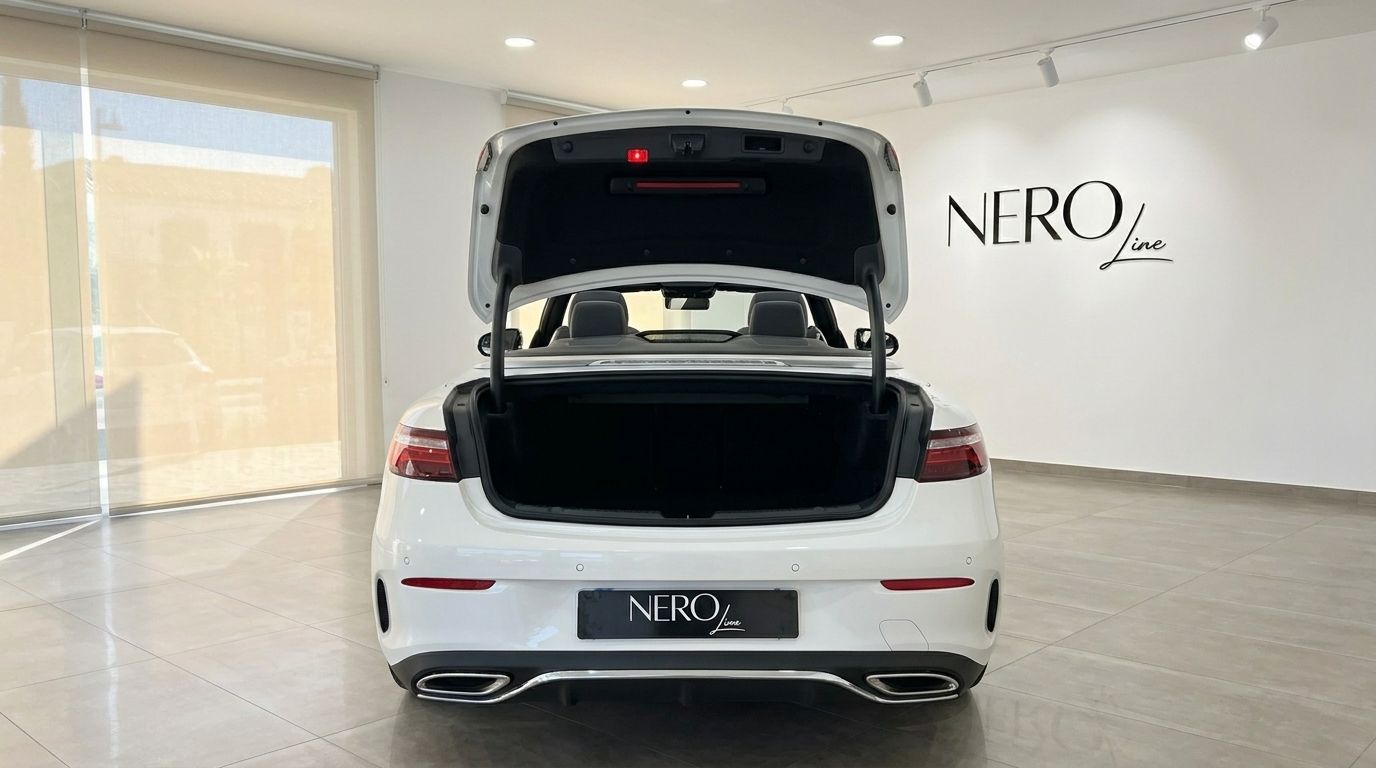La Mercedes-Benz E200 Cabrio blanche est montrée de l'arrière avec son coffre ouvert, garée à l'intérieur à Marbella.