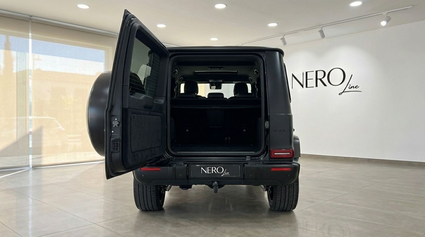 Le Mercedes-Benz G63 AMG noir mat est présenté de l'arrière avec sa porte de coffre ouverte, révélant la zone de chargement spacieuse dans un showroom de Marbella.