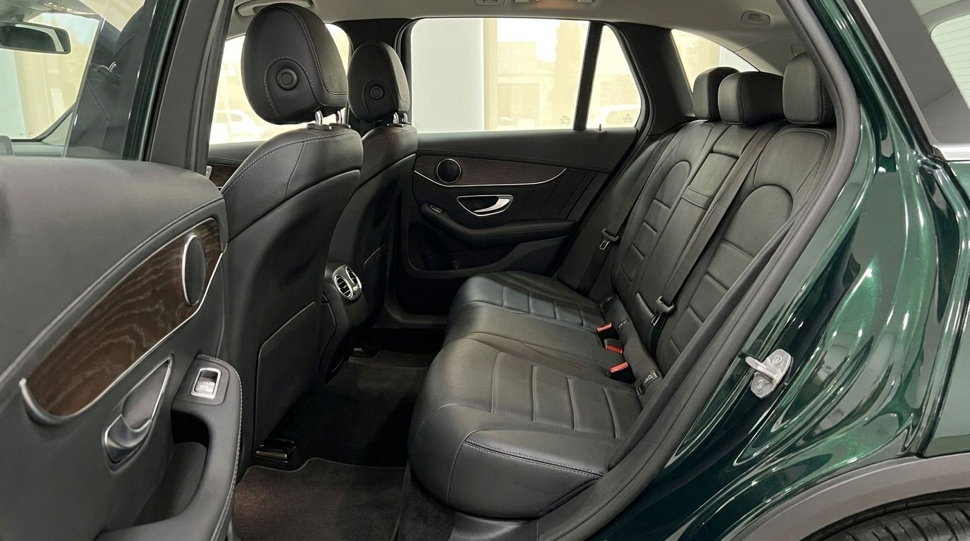The rear passenger compartment of the Mercedes-Benz GLC in Gloss Emerald Green, featuring black leather seats and wood trim, available in Mallorca.