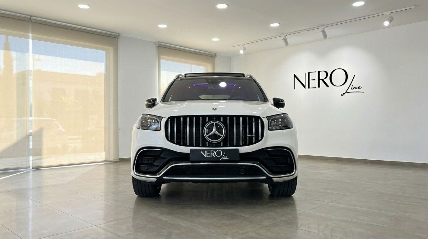 The white 2024 Mercedes-Benz GLS 63 AMG is showcased head-on in a showroom in Alicante, highlighting its prominent grille.