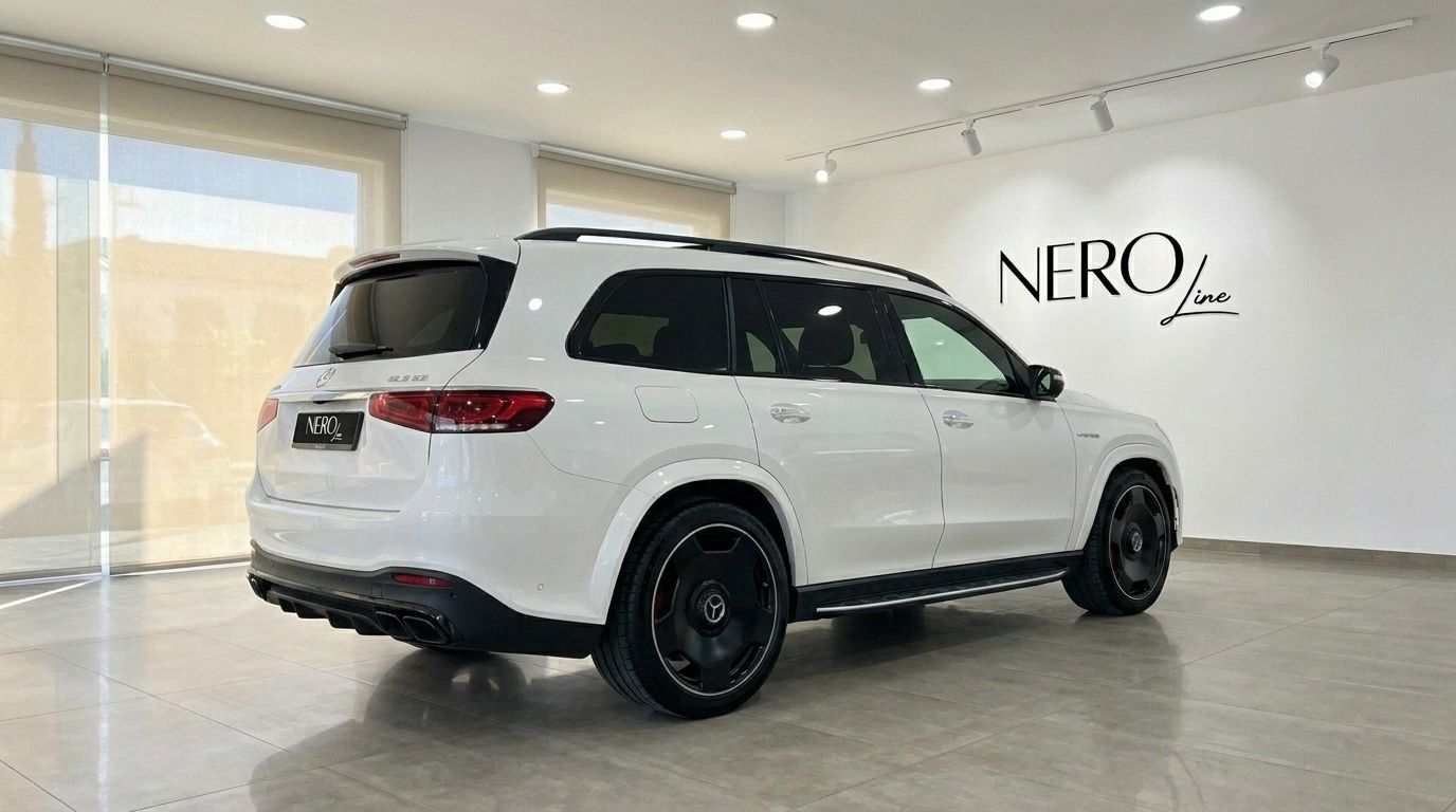 The white 2024 Mercedes-Benz GLS 63 AMG is showcased from a rear three-quarter angle in a showroom in Alicante.