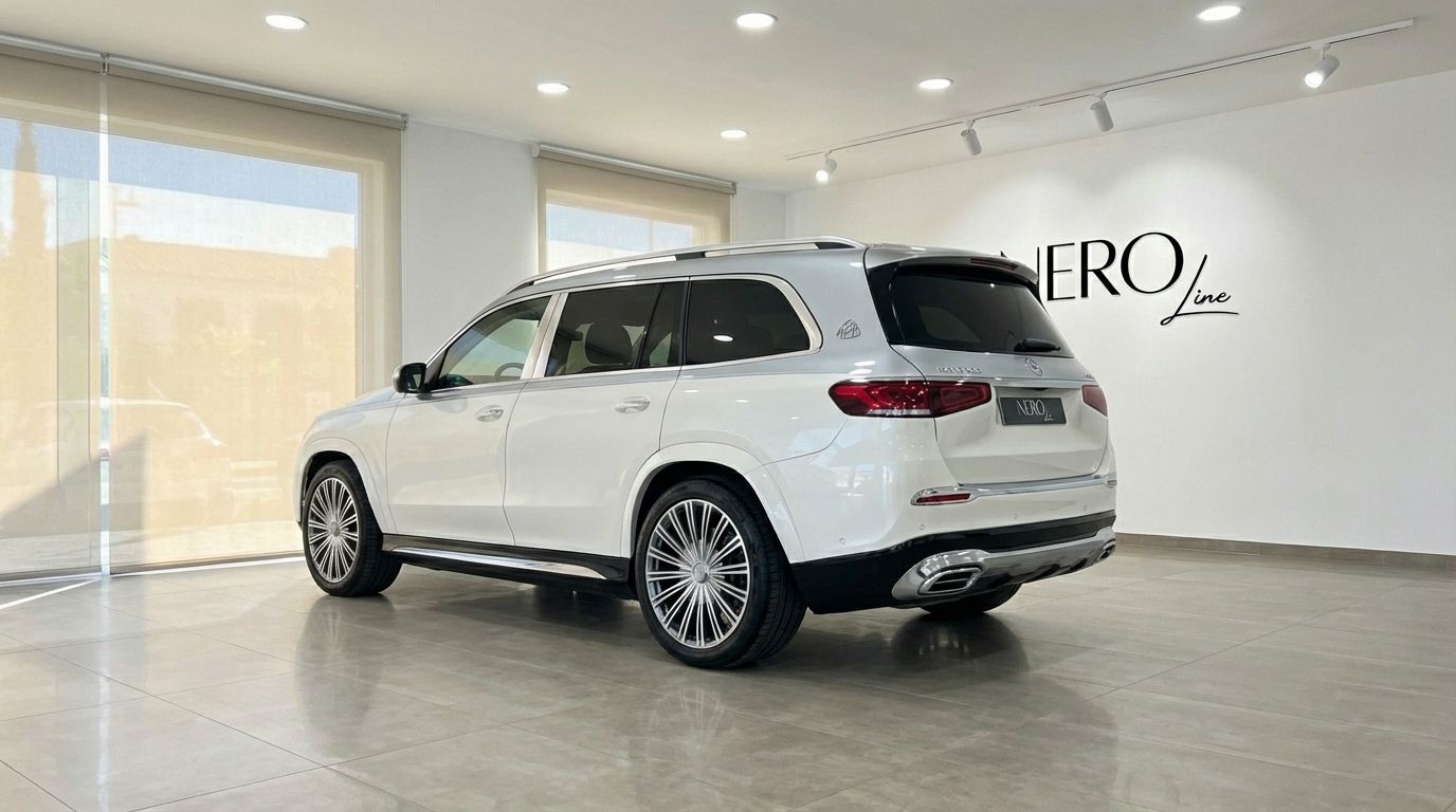 El Mercedes-Benz GLS680 MAYBACH 2024 blanco perla se exhibe desde un ángulo trasero tres cuartos en un showroom de Madrid.