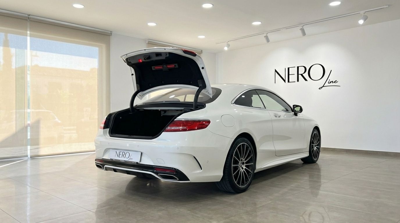 A white Mercedes-Benz S500 Coupe is shown from a rear three-quarter angle with its trunk open inside a showroom in Alicante.