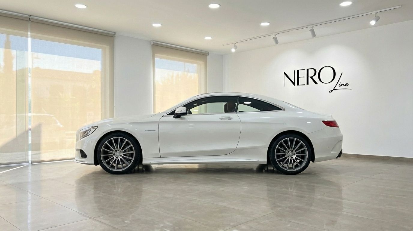 The white Mercedes-Benz S500 Coupe is showcased in a modern showroom, displaying its elegant side profile in Alicante.