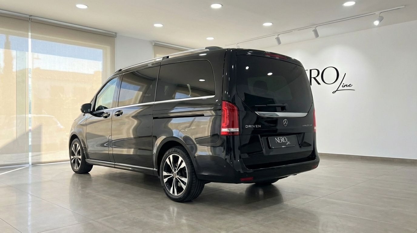 Una furgoneta de lujo Mercedes-Benz V250d negra está estacionada en un ángulo trasero de tres cuartos dentro de una moderna sala de exposición en Madrid.
