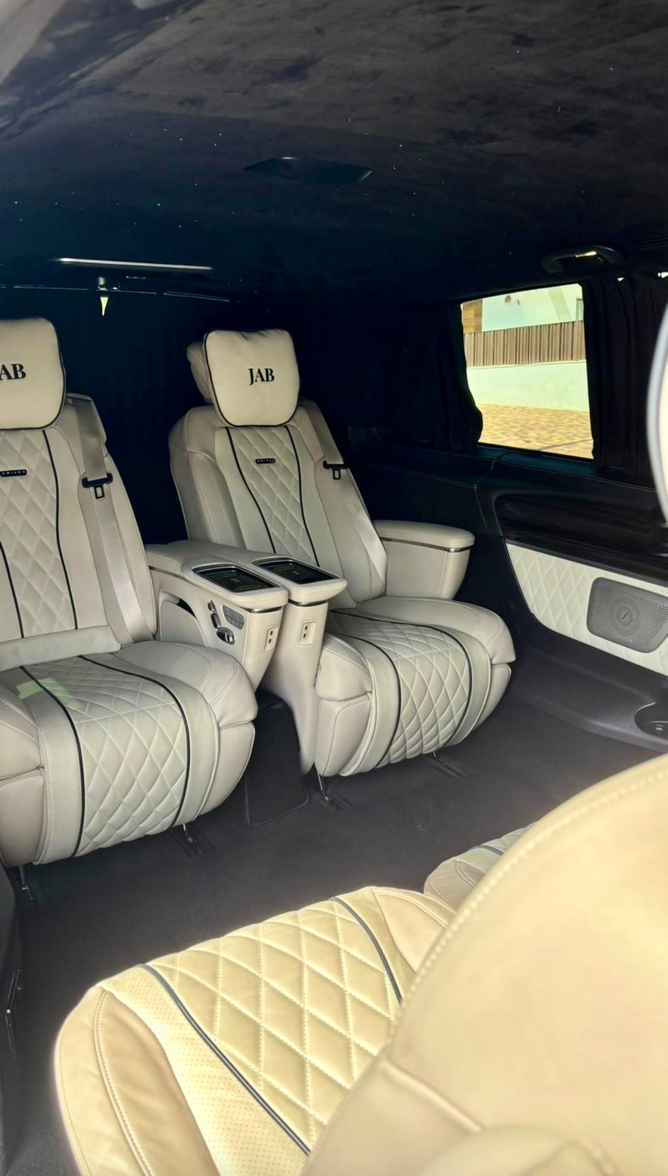 El lujoso interior trasero del Mercedes-Benz V250d DRIVEN - LANDJETS VIP en Madrid, con asientos de cuero blanco acolchado y reposacabezas personalizados.