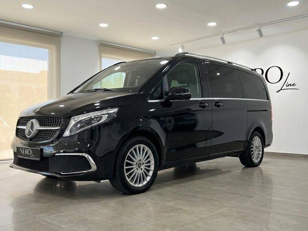 Mercedes-Benz V300 — Furgoneta de Lujo en Madrid Una elegante furgoneta Mercedes-Benz V300 negro obsidiana metálico brillante se exhibe en vista tres cuartos delanteros en un luminoso showroom de Madrid.