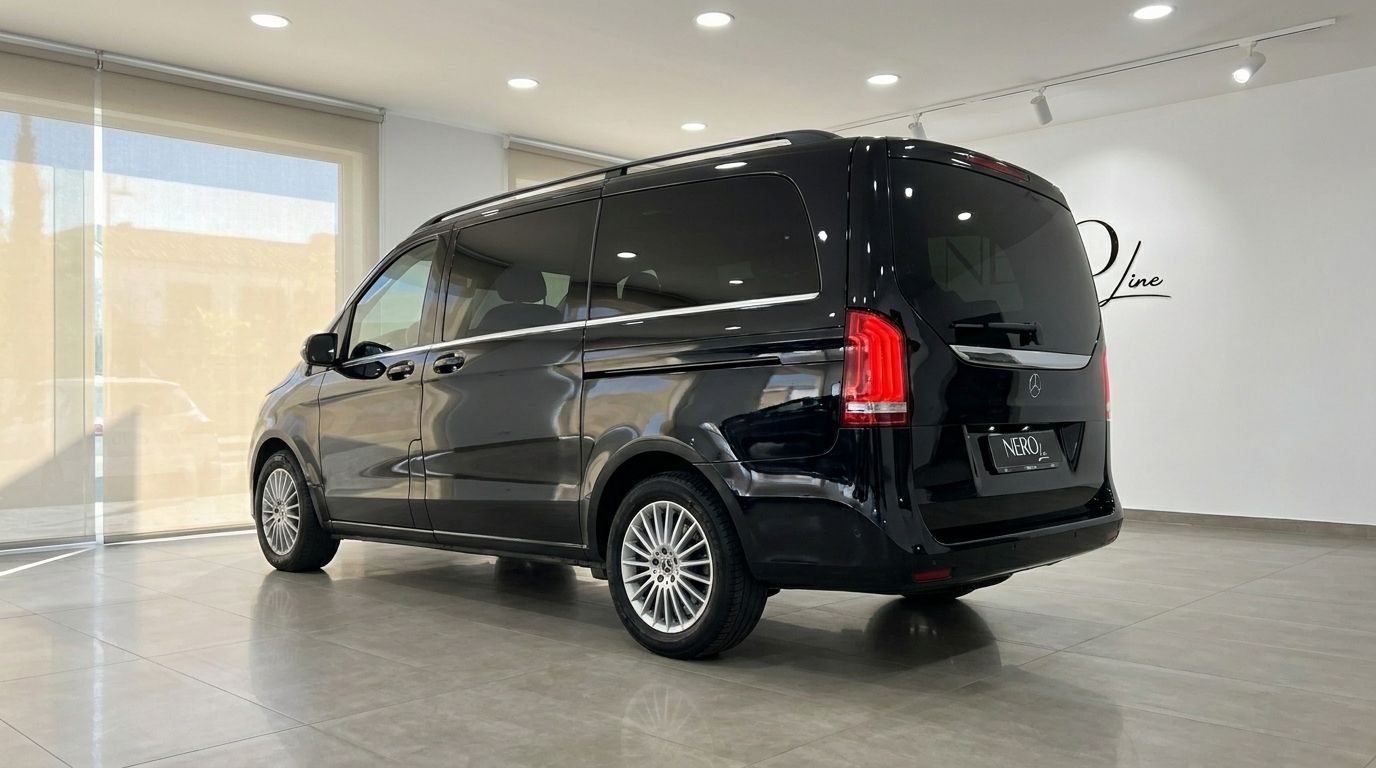 El Mercedes-Benz V300 negro brillante Obsidiana metálico se exhibe desde una vista trasera tres cuartos en un concesionario de Madrid.