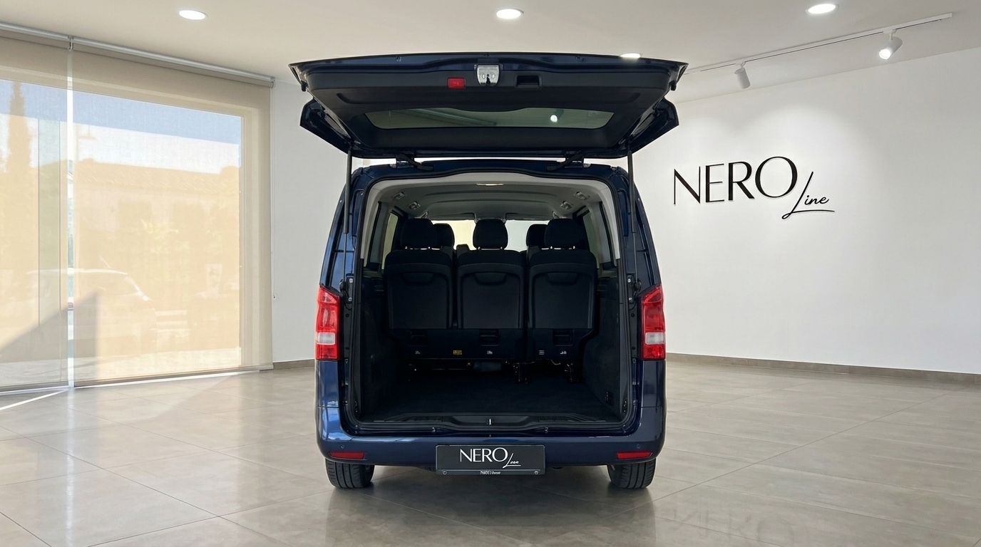 The gloss dark blue Mercedes-Benz Vito Tourer 2026 is shown from the rear with its tailgate open, revealing the spacious interior and seating in a showroom.