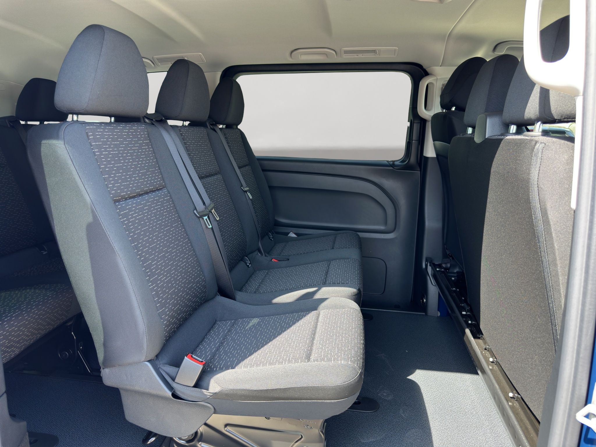 The spacious interior of the Mercedes-Benz Vito Tourer shows multiple rows of dark fabric passenger seats with seatbelts.