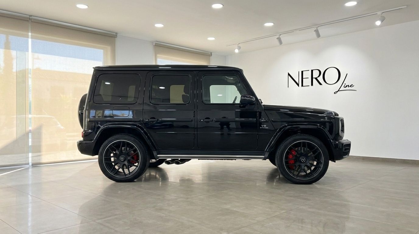 A glossy black 2025 Mercedes G63 AMG SUV is parked sideways in a bright, modern showroom in Madrid.