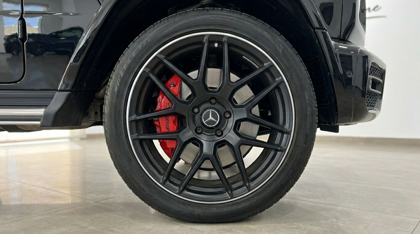 The glossy black Mercedes G63 AMG's front wheel, showcasing its black multi-spoke rim and vibrant red AMG brake caliper in Madrid.