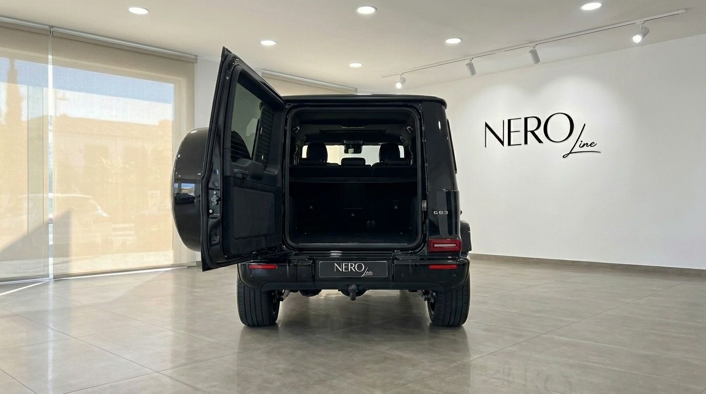 The glossy black Mercedes G63 AMG is shown from the rear with its trunk open, revealing ample cargo space in Madrid.