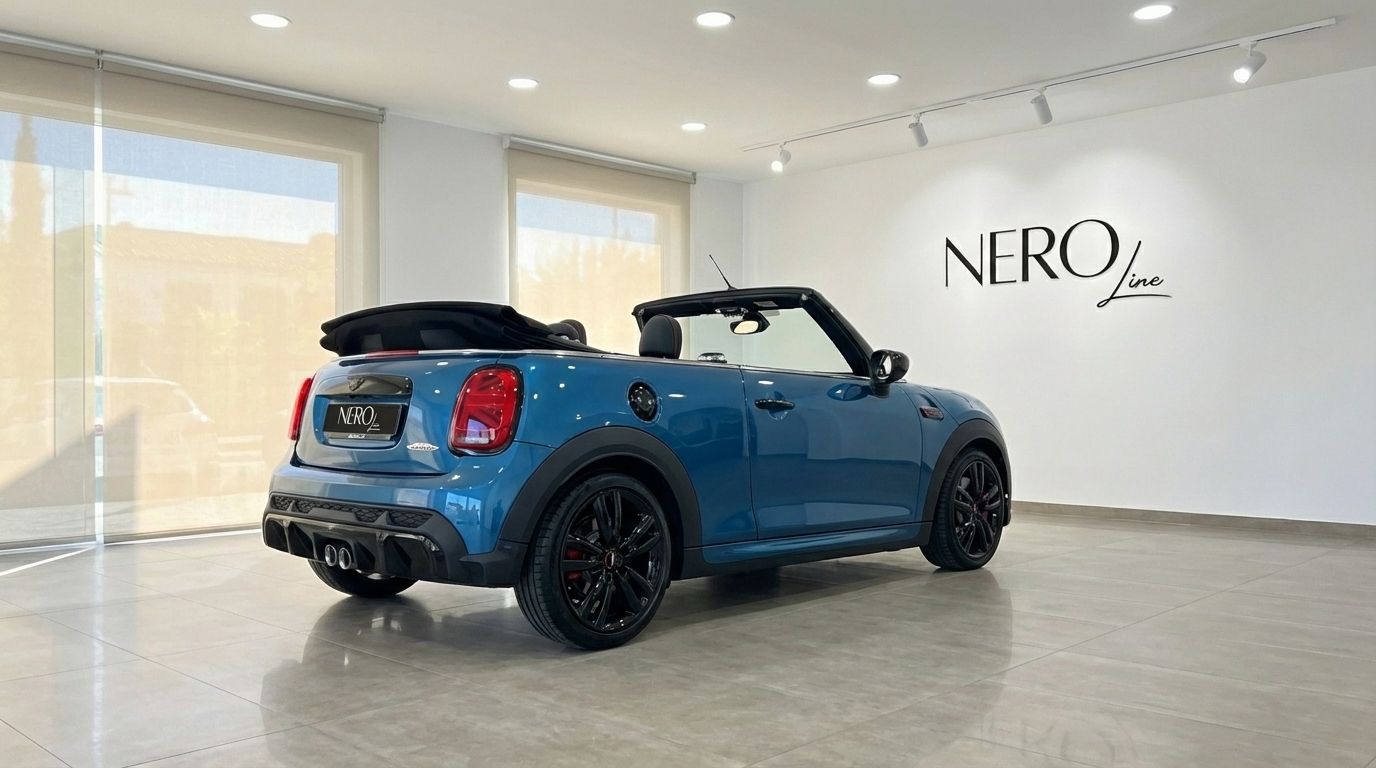 Metallic blue Mini Cooper John Works Convertible, roof down, displayed from the rear three-quarter angle in an Ibiza showroom.