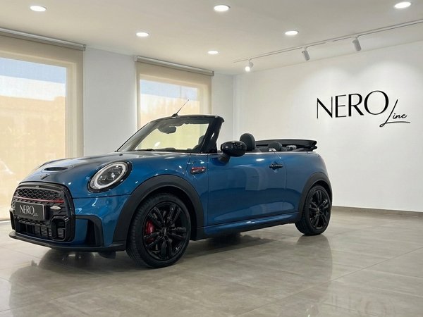 Mini Cooper John Works Convertible — Showroom Ibiza The metallic blue Mini Cooper John Works Convertible is showcased from a front three-quarter angle with its top down in an Ibiza showroom.