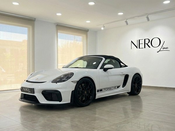 Porsche 718 SPIDER RS — Showroom en Madrid Porsche 718 SPIDER RS descapotable blanco, visto desde el ángulo frontal tres cuartos, estacionado en un moderno concesionario en Madrid.