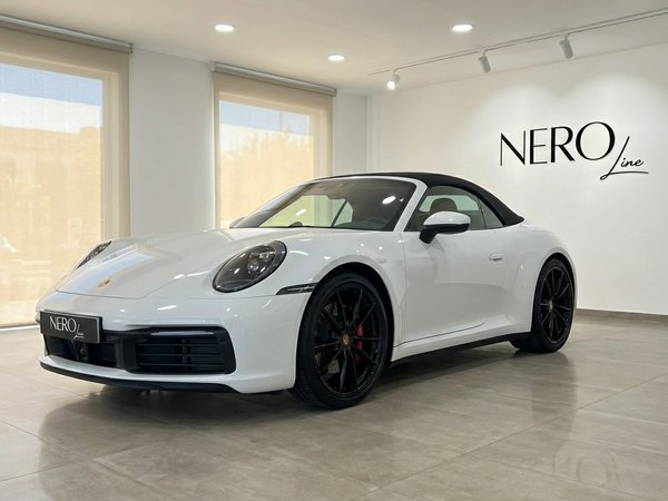 Porsche 911 Carrera S 992 Cabrio — Showroom A white Porsche 911 Carrera S 992 Cabrio convertible is displayed from a front three-quarter view in a Marbella showroom.