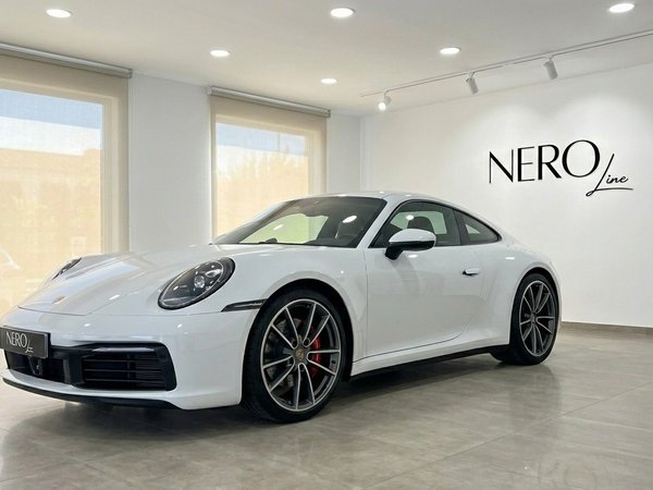 Porsche 911 Carrera S 992 — Showroom à Madrid La Porsche 911 Carrera S 992 (Coupé) blanche est présentée de trois quarts avant dans un showroom lumineux à Madrid.