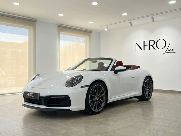 Porsche 911 Carrera S Cabrio 992 — Showroom The white Porsche 911 Carrera S Cabrio 992 convertible is showcased from a front three-quarter angle in a bright Marbella showroom, featuring red interior and the NEROline logo.