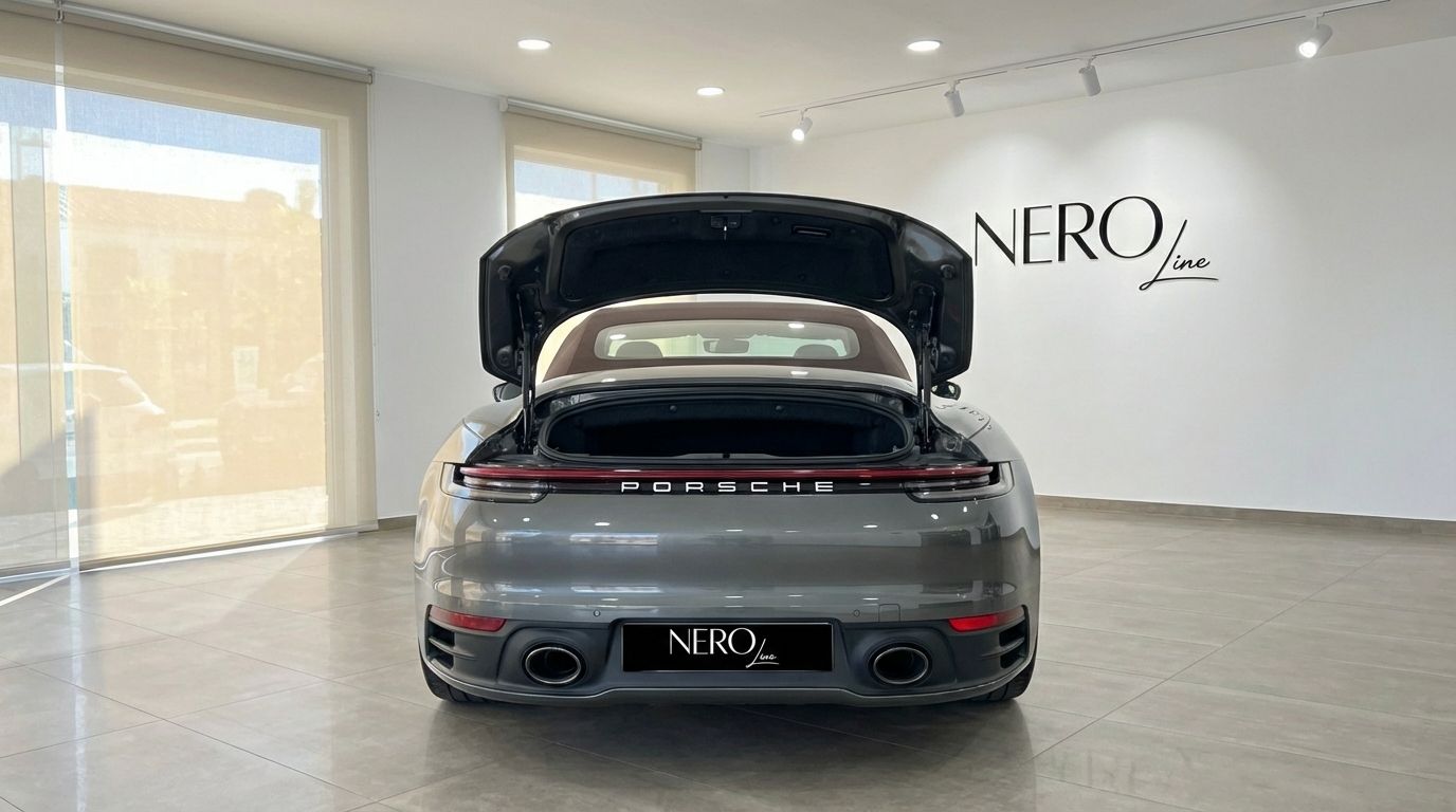The grey Porsche 911 Carrera S Cabrio is shown from the rear with its trunk open, parked in a showroom in Marbella.