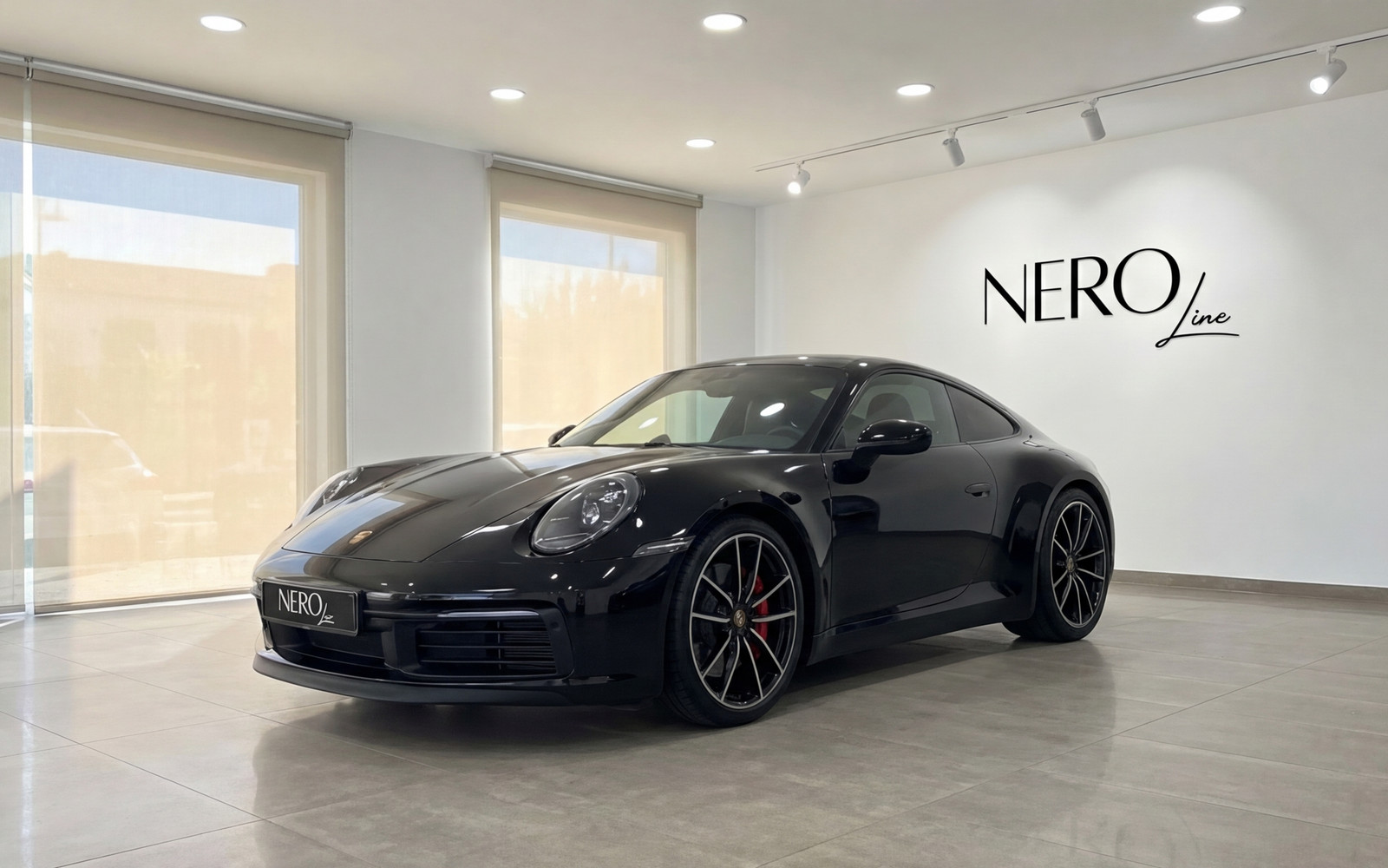 Porsche 911 — Luxury Car in Malaga Showroom A sleek black Porsche 911 is showcased from a front three-quarter angle in a bright Nero Line showroom in Malaga.