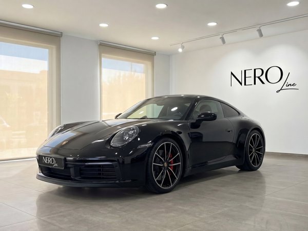 Porsche 911 — Luxury Car in Malaga Showroom A sleek black Porsche 911 is showcased from a front three-quarter angle in a bright Nero Line showroom in Malaga.