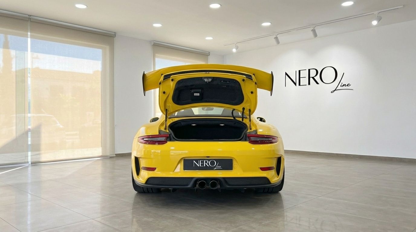 Vista posteriore di una Porsche 911 GT3 RS giallo lucido con il bagagliaio aperto, parcheggiata in uno showroom moderno a Ibiza.