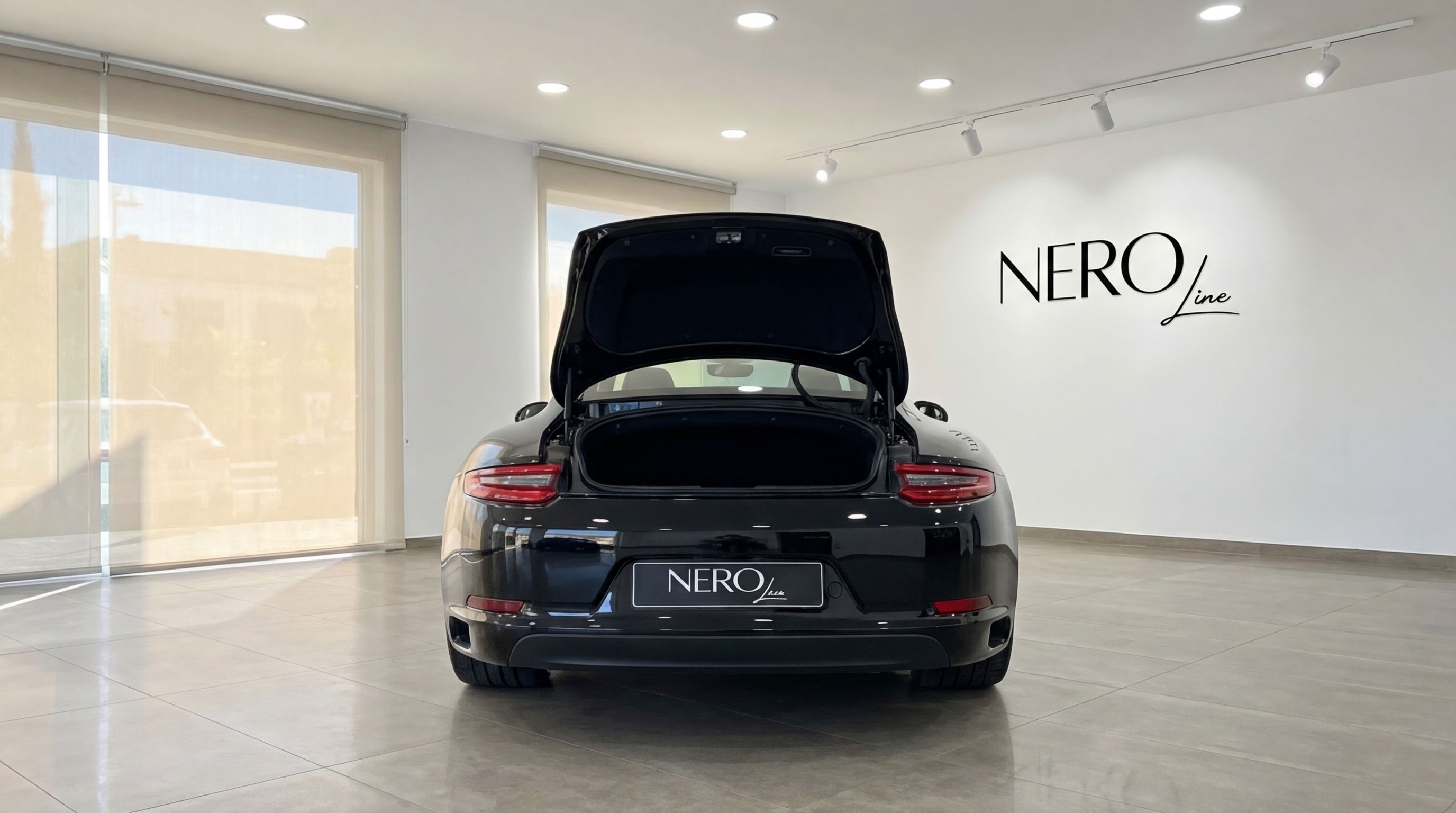The black Porsche 911 is seen from the rear with its trunk open, parked inside a luxury showroom in Malaga.