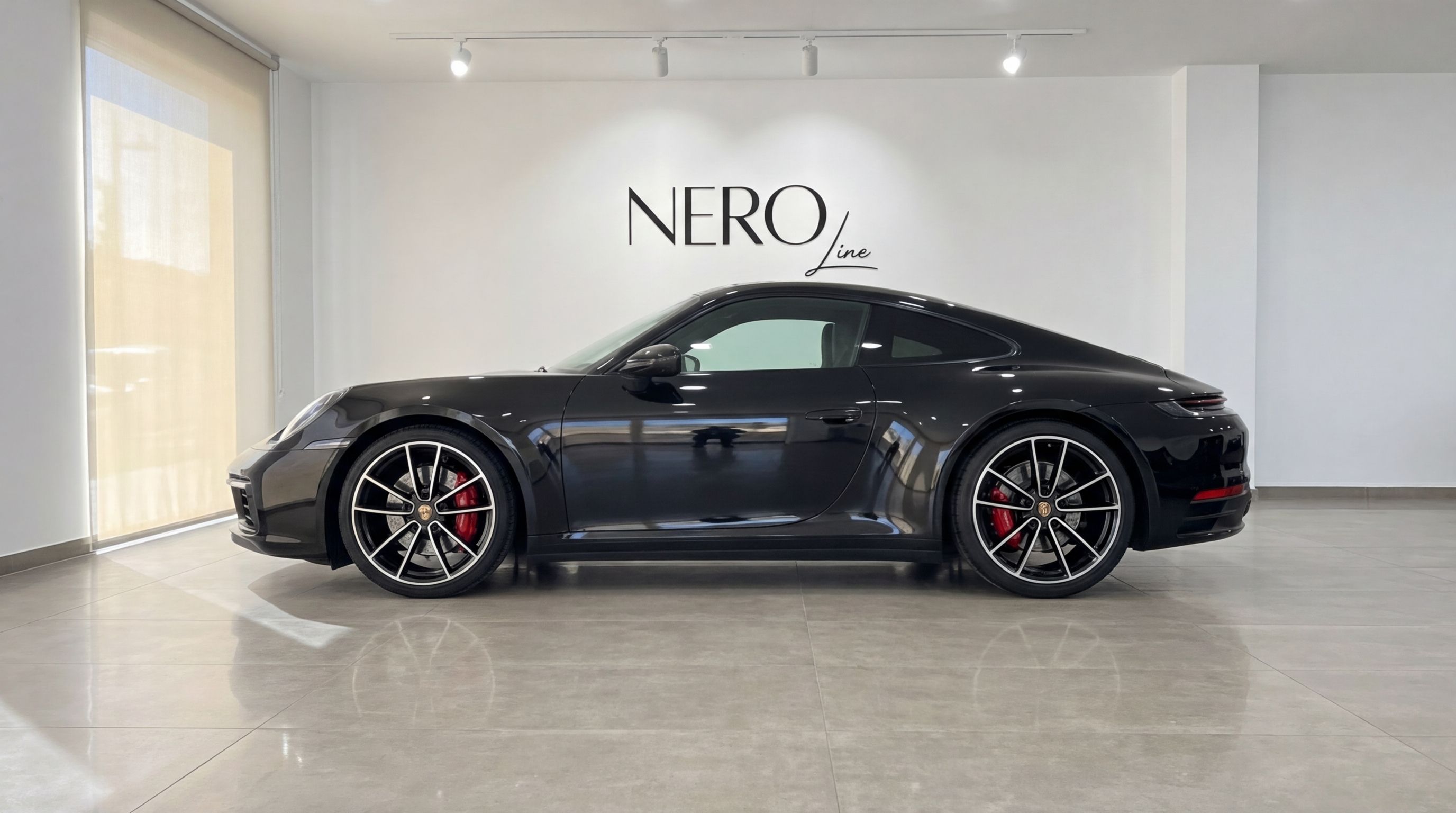 A sleek black Porsche 911 is showcased in a side profile view inside a modern showroom in Malaga.