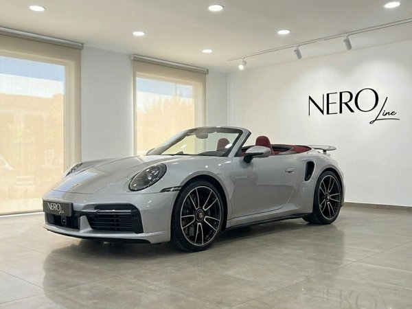 Porsche 911 Turbo S Cabriolet — Barcelona showroom The silver 2023 Porsche 911 Turbo S Cabriolet with a red interior is showcased from the front three-quarter view in a Barcelona showroom.