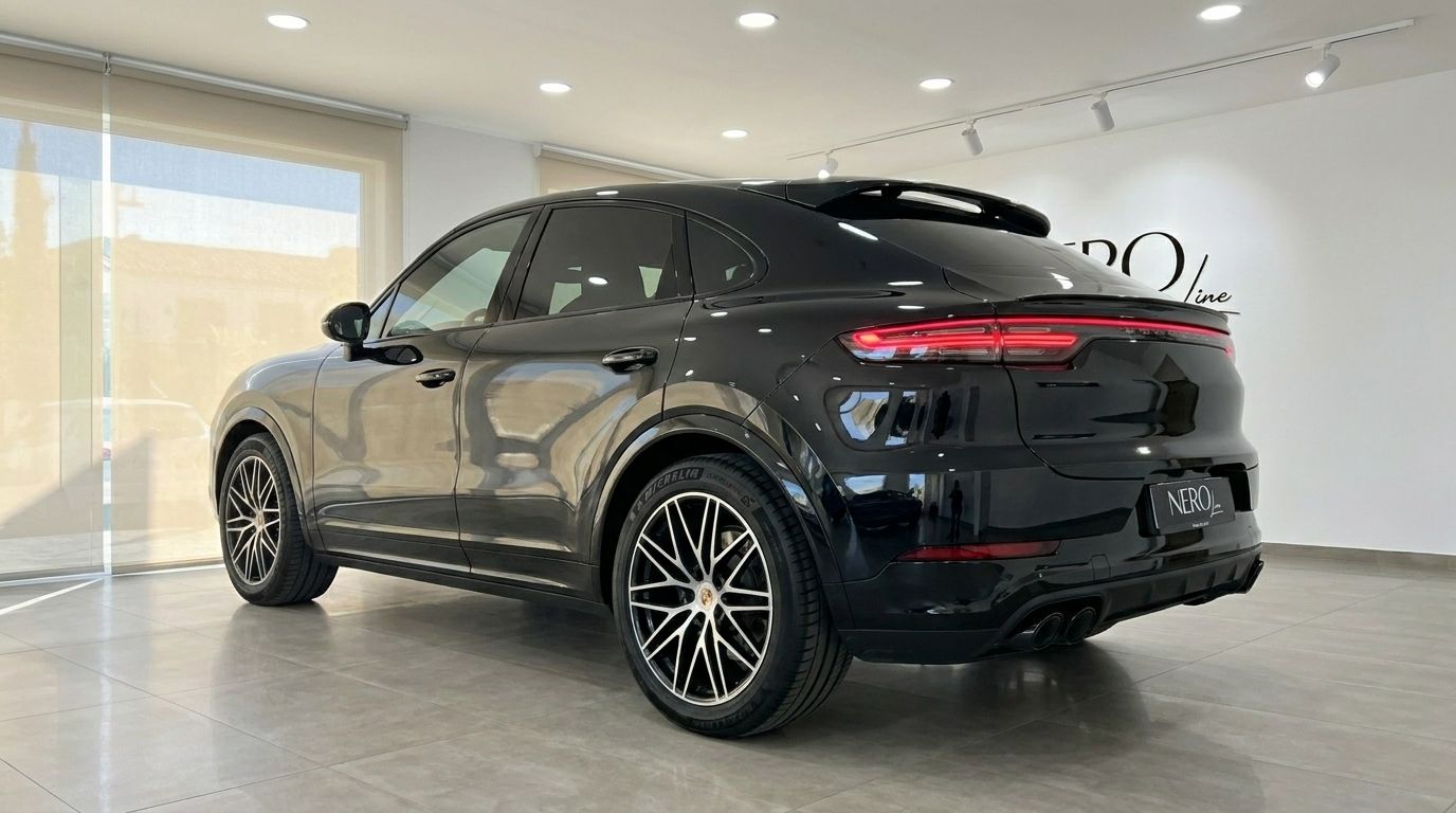 A sleek black Porsche Cayenne is showcased from a rear three-quarter angle in a modern showroom in Alicante.